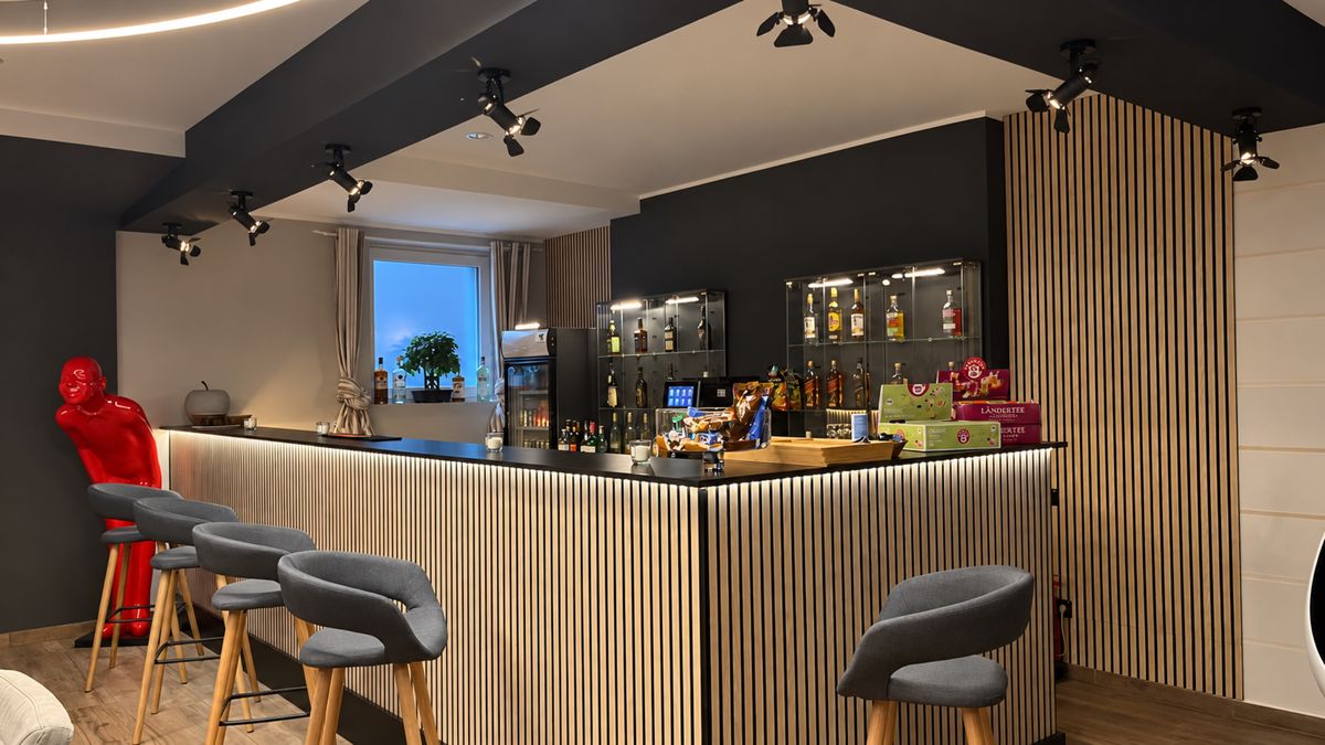 Hotelbar mit Lamellenverkleidung, Barhockern und beleuchteten Regalen