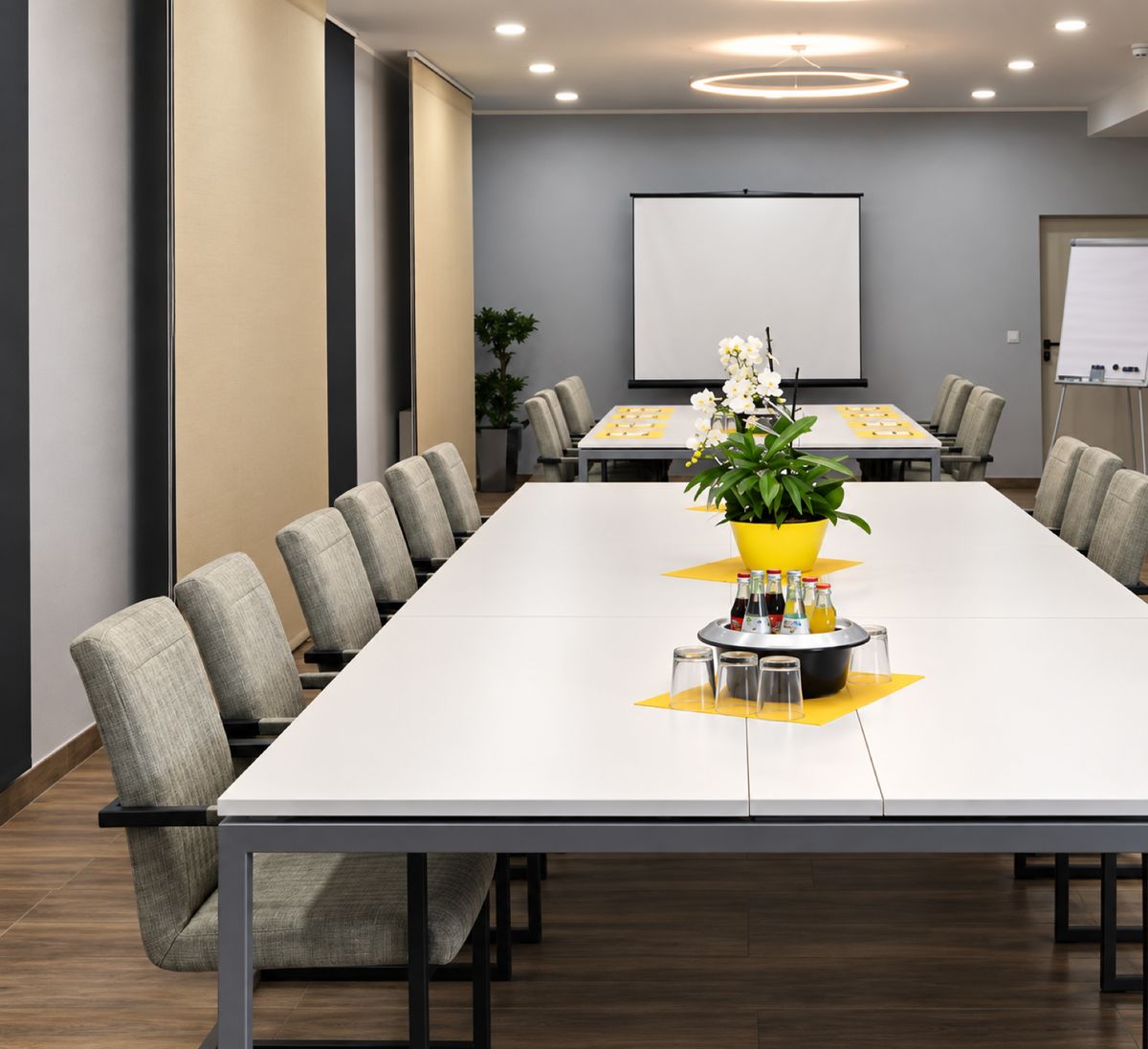 Meeting Room mit langer weißer Konferenztafel, Stühlen und Präsentationswand