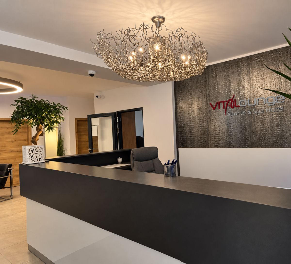 Rezeption des Hotels mit Kronleuchter und VitaLounge-Logo an der Wand