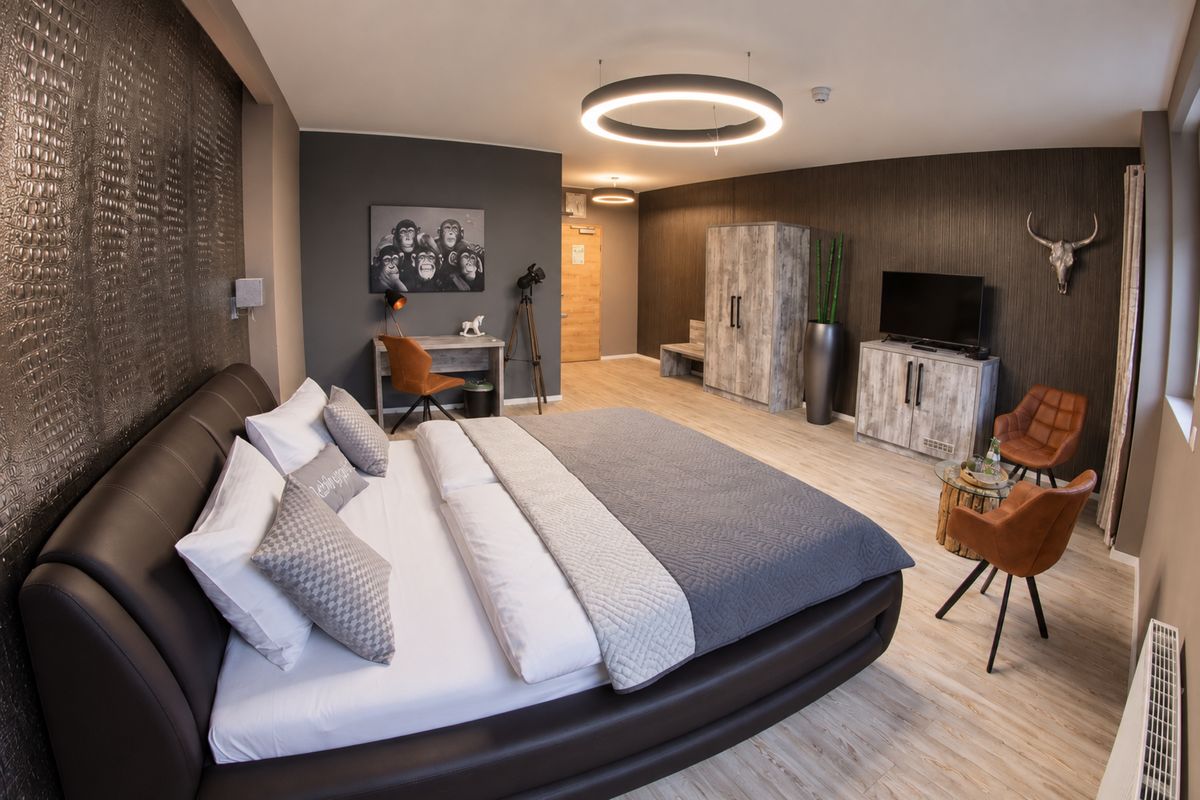 Doppelzimmer im VitaLounge Hotel: Boxspringbett mit Kissen, Lichtring an der Decke, Sessel aus Cognac-Leder