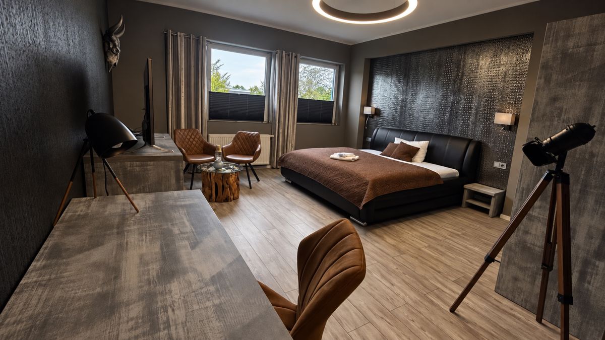 Juniorsuite mit Queensize-Bett, Sitzecke, Stehlampe im Stativ-Design und großen Fenstern