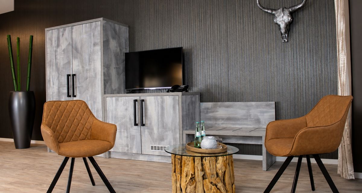 Standard-Doppelzimmer mit TV-Sideboard aus grauem Holz und zwei Sesseln aus Cognac-Leder